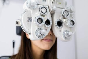 Adult reading near a window while covering one eye during a vision check with an eye-care professional.